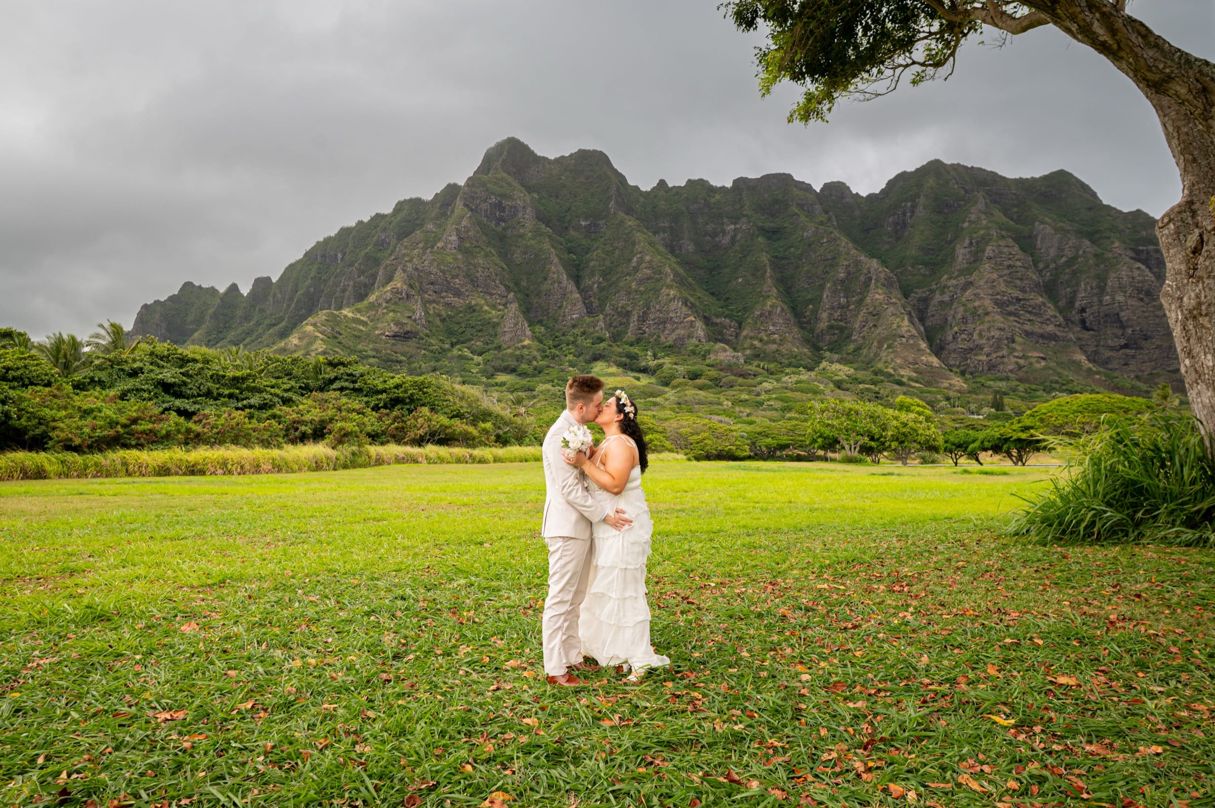 A couple sharing a kiss on the lawn at Kualoa after their elopement ceremony, the mountains behind them