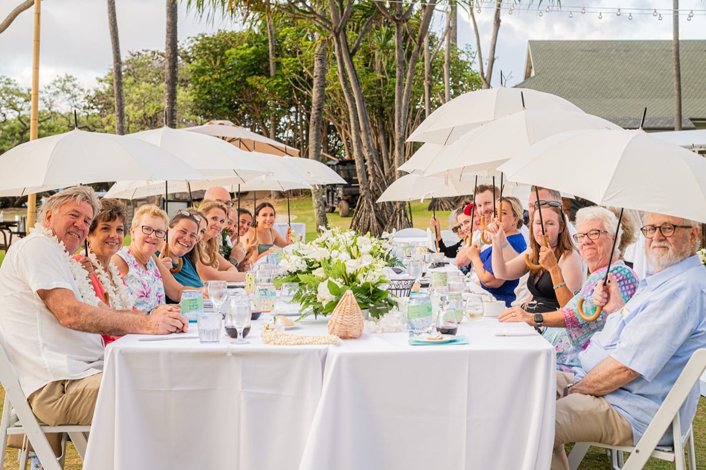 Guests under white umbrellas at the lawn dinner while a shower passes